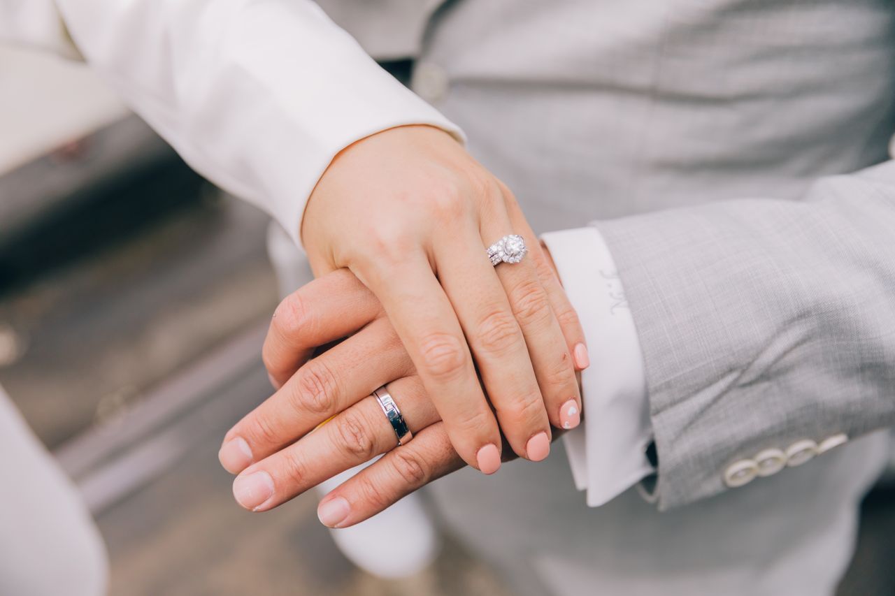 Close-up of intertwined hands displaying elegant wedding and engagement rings.